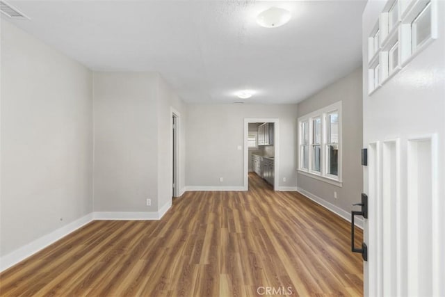 empty room featuring dark wood-style floors, visible vents, and baseboards