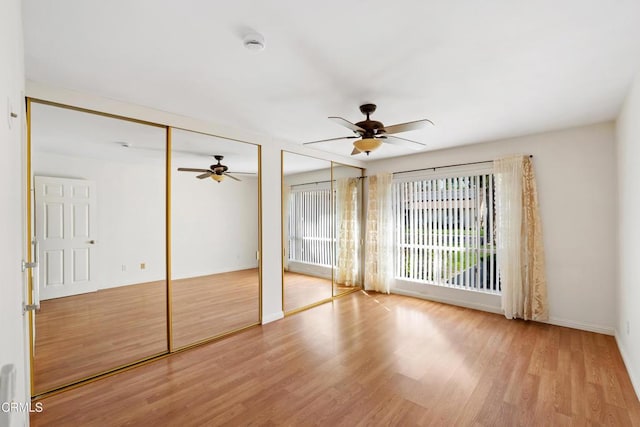 unfurnished bedroom with baseboards, wood finished floors, a ceiling fan, and multiple closets