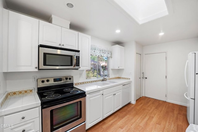 kitchen featuring white cabinetry, tile counters, stainless steel appliances, and a sink