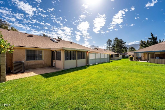 back of house with stucco siding, fence, central AC unit, and a yard