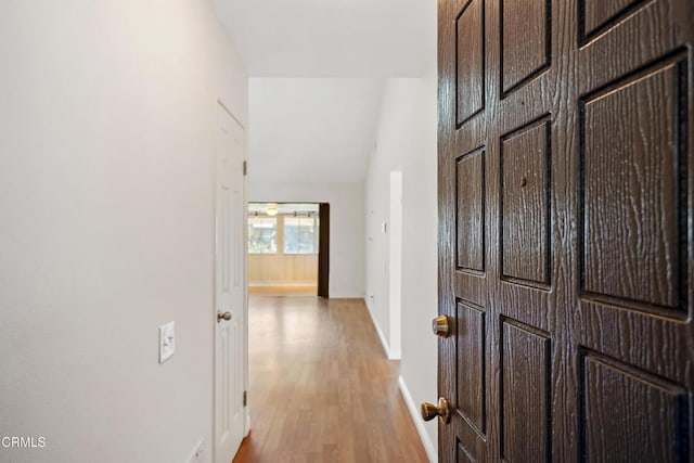 hall featuring lofted ceiling, light wood-style flooring, and baseboards