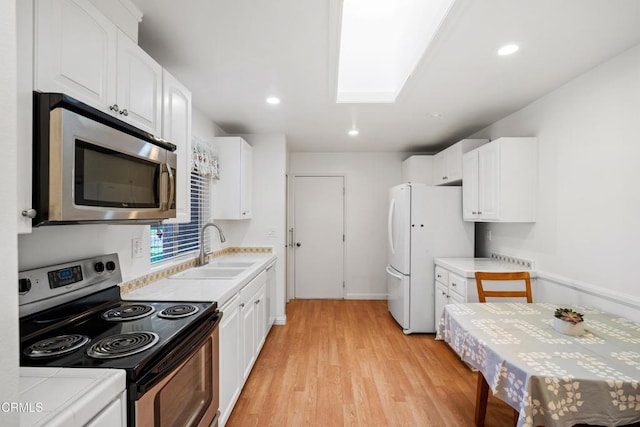 kitchen with a skylight, light wood finished floors, stainless steel appliances, white cabinetry, and a sink