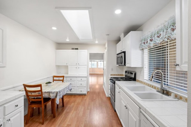 kitchen featuring a sink, white cabinets, appliances with stainless steel finishes, light wood-type flooring, and tile counters