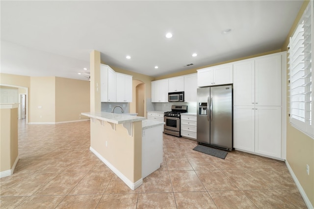 kitchen with light tile patterned floors, a peninsula, a breakfast bar, white cabinets, and appliances with stainless steel finishes