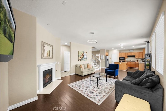 living room featuring recessed lighting, dark wood finished floors, baseboards, stairway, and a glass covered fireplace