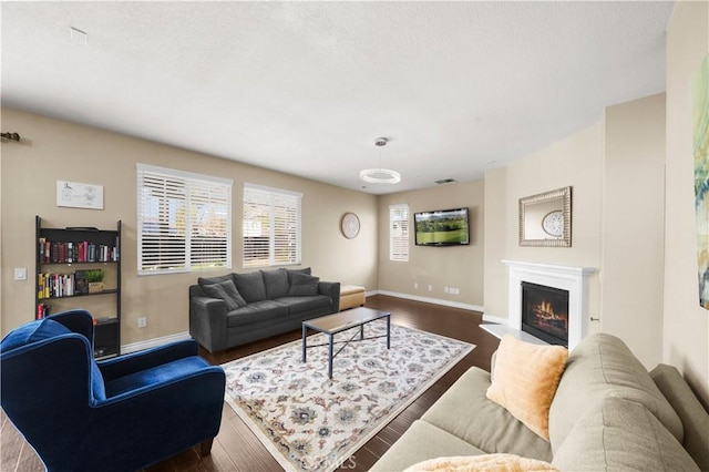 living room with dark wood-style floors, a fireplace with flush hearth, visible vents, and baseboards