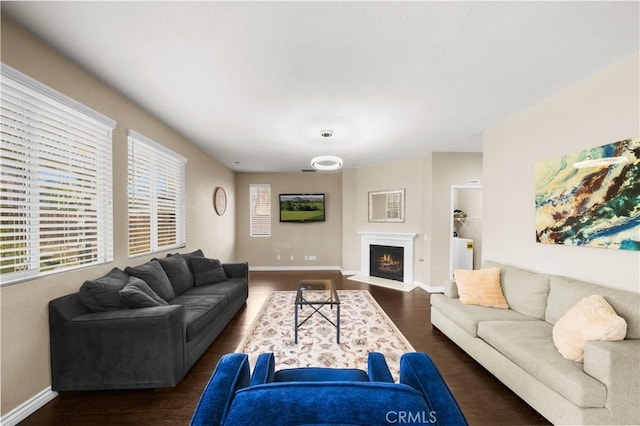 living room featuring a fireplace with flush hearth, baseboards, and dark wood finished floors