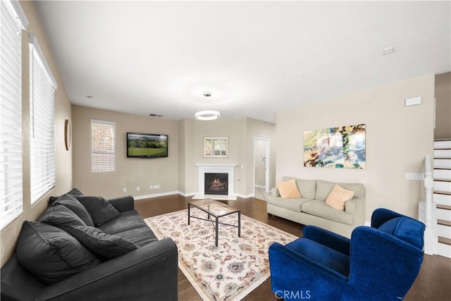 living area with a warm lit fireplace, baseboards, and dark wood-type flooring