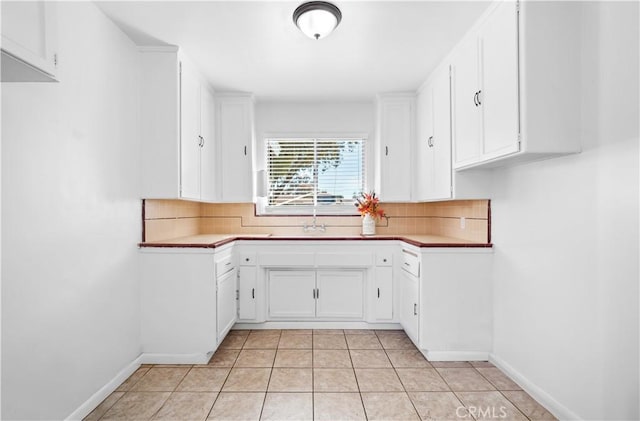 kitchen with white cabinetry, a sink, decorative backsplash, and light tile patterned flooring