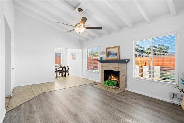 unfurnished living room featuring lofted ceiling with beams, a tiled fireplace, a ceiling fan, light wood-type flooring, and baseboards