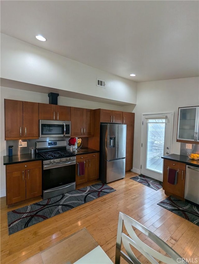 kitchen with visible vents, appliances with stainless steel finishes, light wood-type flooring, dark countertops, and glass insert cabinets