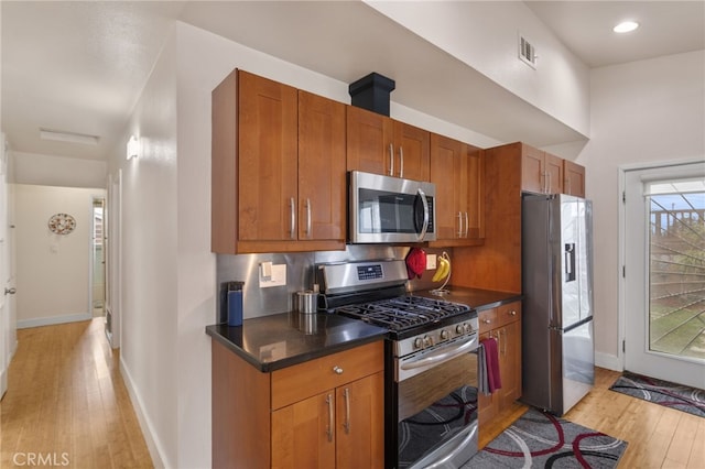 kitchen featuring stainless steel appliances, dark countertops, brown cabinetry, light wood-style floors, and baseboards