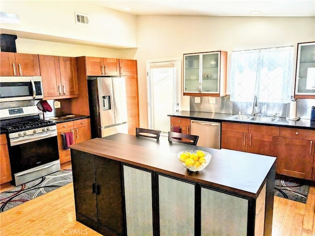 19309 Tillman Ave, Carson, CA 90746 - kitchen featuring appliances with stainless steel finishes, light wood-style flooring, dark countertops, glass insert cabinets, and brown cabinets
