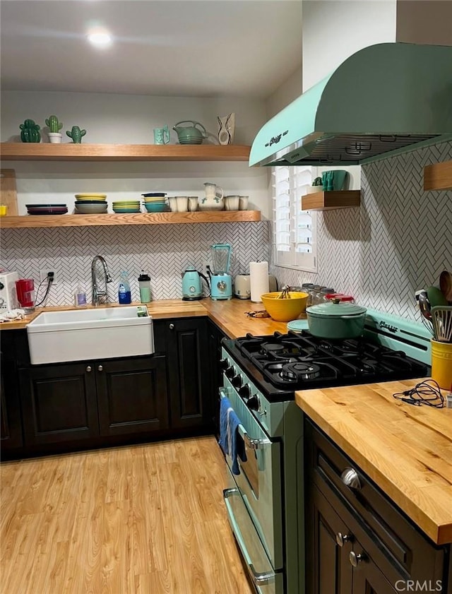 kitchen with butcher block counters, stainless steel range with gas stovetop, open shelves, a sink, and exhaust hood