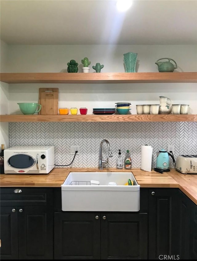 kitchen featuring dark cabinetry, a sink, wood counters, and open shelves