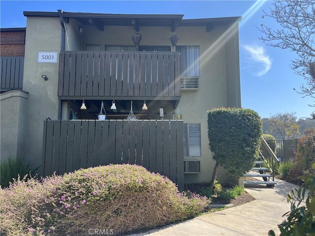 view of side of home featuring a balcony, fence, and stucco siding