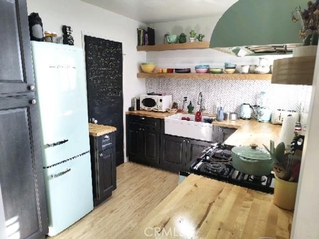 kitchen featuring open shelves, decorative backsplash, a sink, light wood-type flooring, and fridge