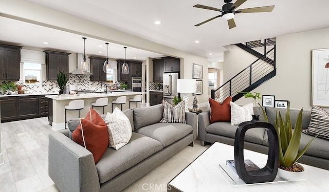 living area with recessed lighting, a ceiling fan, baseboards, stairway, and light wood finished floors