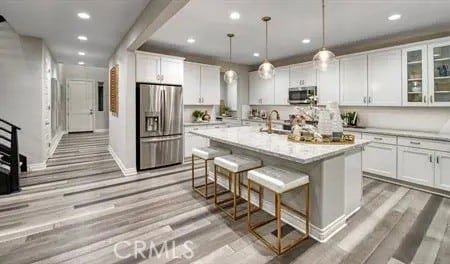 kitchen featuring pendant lighting, a breakfast bar area, stainless steel appliances, white cabinets, and a kitchen island with sink