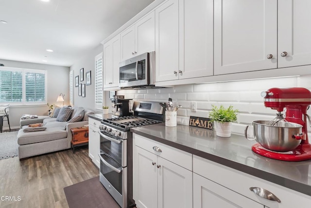 kitchen featuring dark wood-style floors, dark countertops, appliances with stainless steel finishes, open floor plan, and white cabinetry