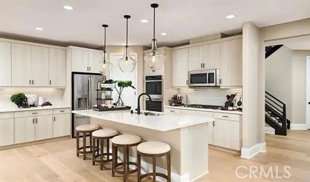 kitchen with stainless steel appliances, white cabinetry, light countertops, a center island with sink, and pendant lighting