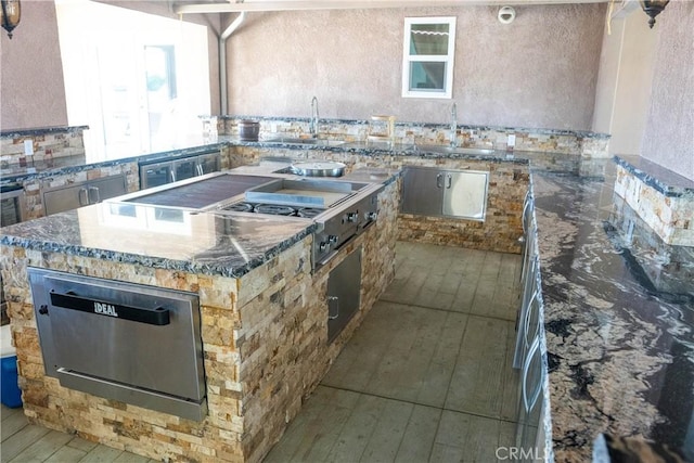 kitchen featuring light wood finished floors, a kitchen island, dark stone countertops, a sink, and a warming drawer