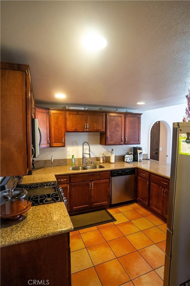 kitchen featuring light stone counters, appliances with stainless steel finishes, arched walkways, and a sink