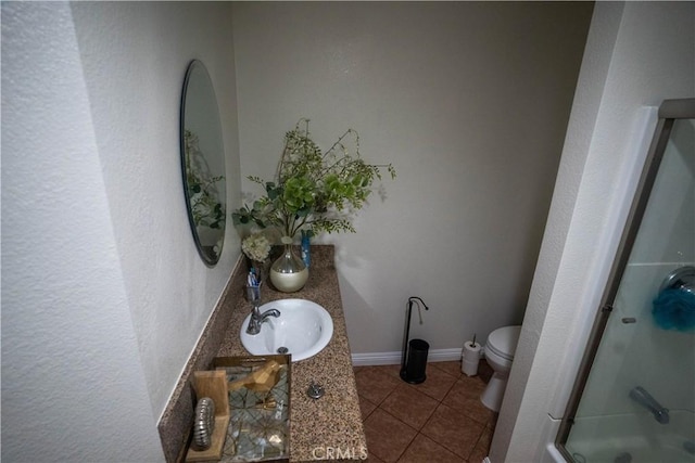 bathroom with toilet, a shower with shower door, vanity, baseboards, and tile patterned floors