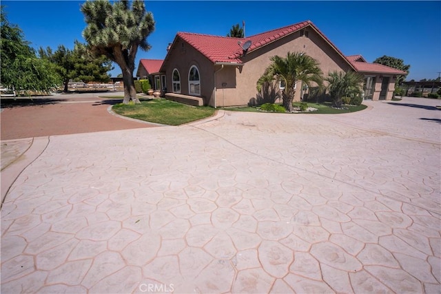 view of side of property with decorative driveway, a tile roof, and stucco siding