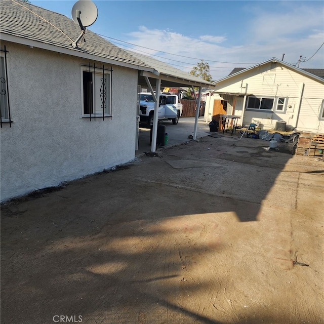 view of side of home with a carport, a shingled roof, and stucco siding