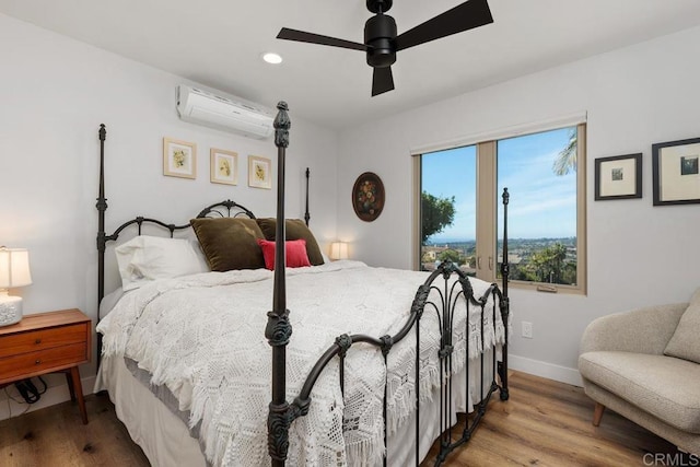 bedroom featuring ceiling fan, baseboards, an AC wall unit, and wood finished floors