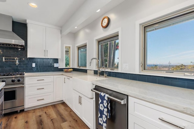 kitchen featuring a sink, white cabinets, appliances with stainless steel finishes, light stone countertops, and wall chimney exhaust hood