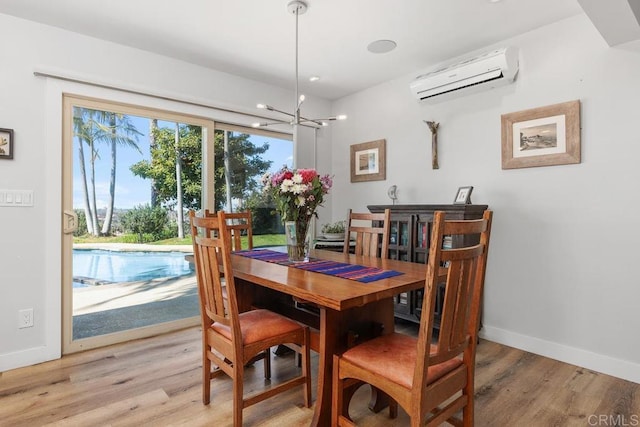 dining space with a chandelier, an AC wall unit, baseboards, and light wood finished floors