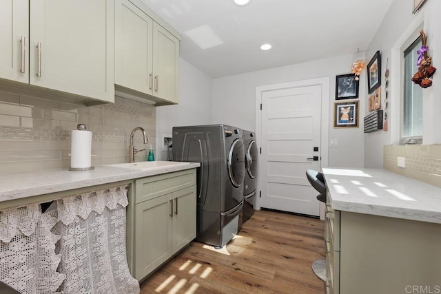 clothes washing area with washing machine and dryer, recessed lighting, wood finished floors, a sink, and cabinet space