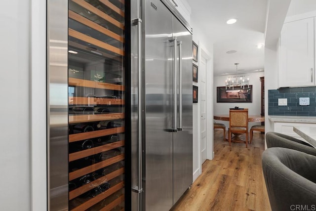 kitchen featuring wine cooler, light wood finished floors, light countertops, hanging light fixtures, and white cabinetry