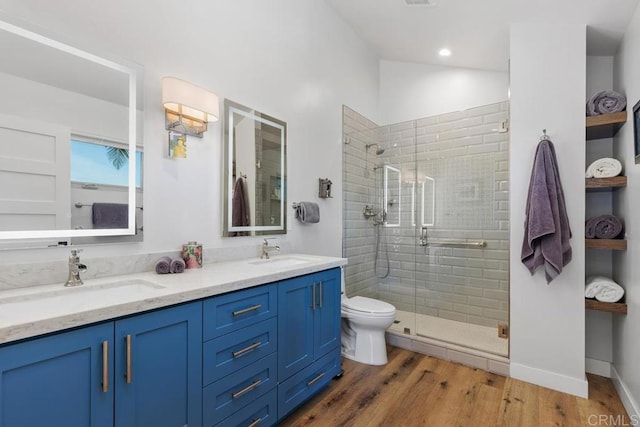 bathroom with double vanity, wood finished floors, a sink, and a shower stall