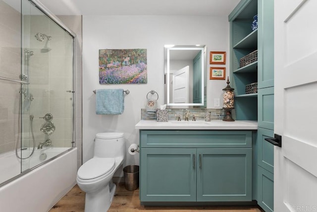 bathroom featuring toilet, wood finished floors, combined bath / shower with glass door, vanity, and backsplash