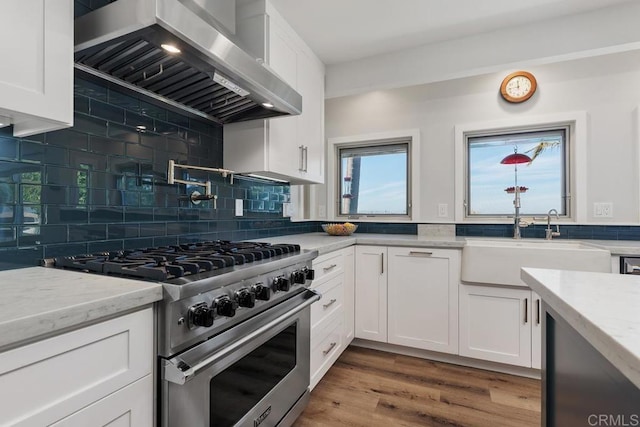 kitchen with high end stove, white cabinetry, a sink, and exhaust hood