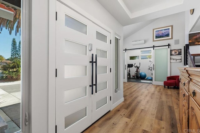 foyer entrance featuring light wood-type flooring, a barn door, and vaulted ceiling