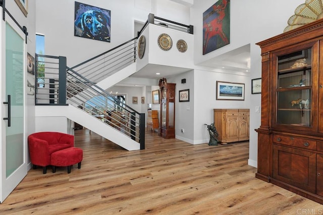 foyer featuring a barn door, a high ceiling, baseboards, stairs, and light wood-type flooring