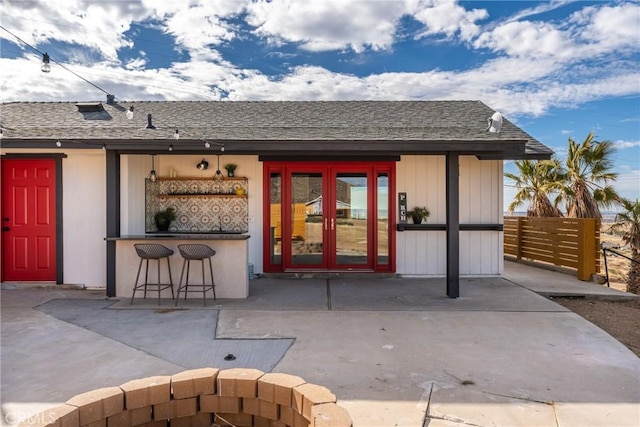 doorway to property with outdoor dry bar, a shingled roof, a patio area, and fence