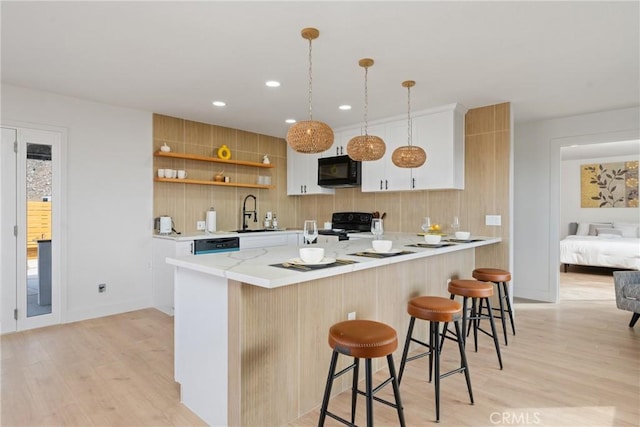 kitchen with black appliances, a kitchen bar, open shelves, and light wood-style floors