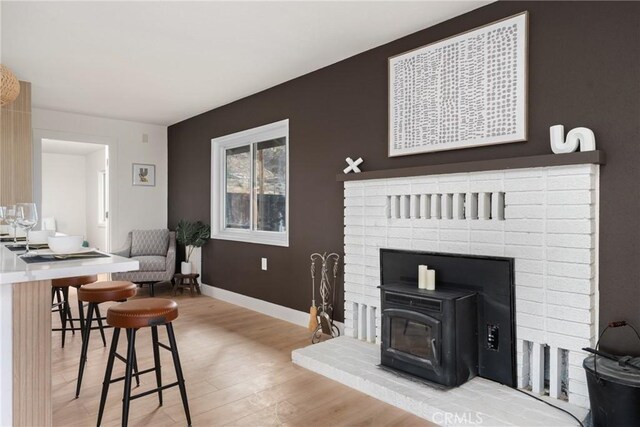 living room with a wood stove, light wood-style flooring, and baseboards