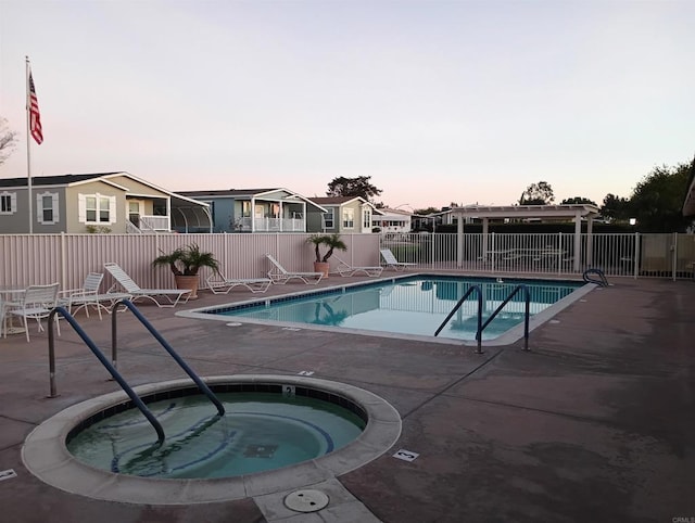 pool at dusk featuring a patio, a residential view, a community pool, fence, and a community hot tub