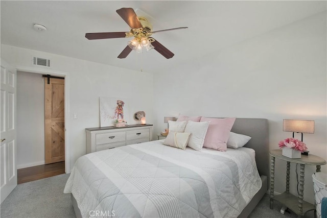 bedroom with a barn door, visible vents, and a ceiling fan