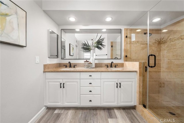 full bath with double vanity, a stall shower, a sink, and wood finished floors