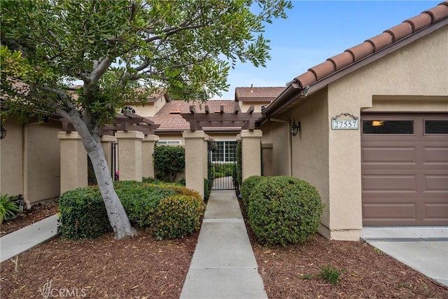 doorway to property with a garage, a tile roof, a gate, and stucco siding