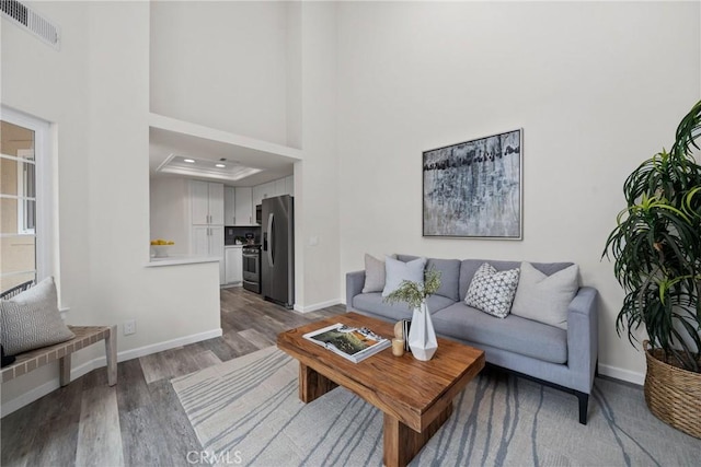 living room featuring a towering ceiling, baseboards, visible vents, and wood finished floors