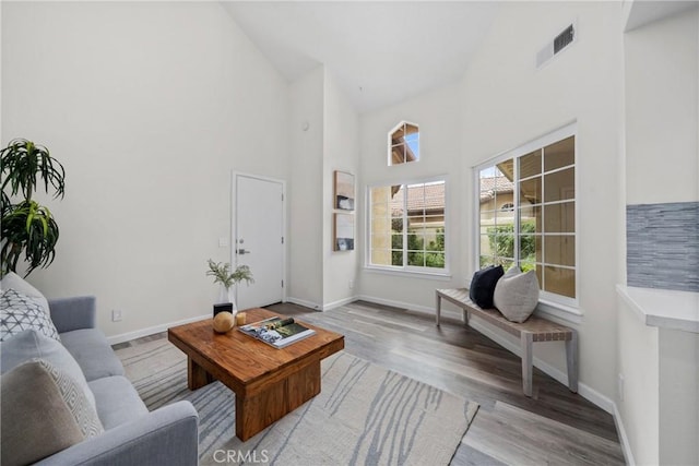 living room with a high ceiling, visible vents, light wood-style flooring, and baseboards