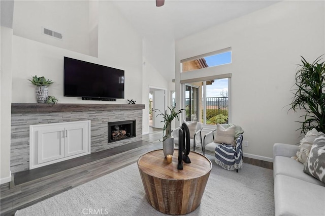 living area with baseboards, visible vents, a tile fireplace, a towering ceiling, and wood finished floors